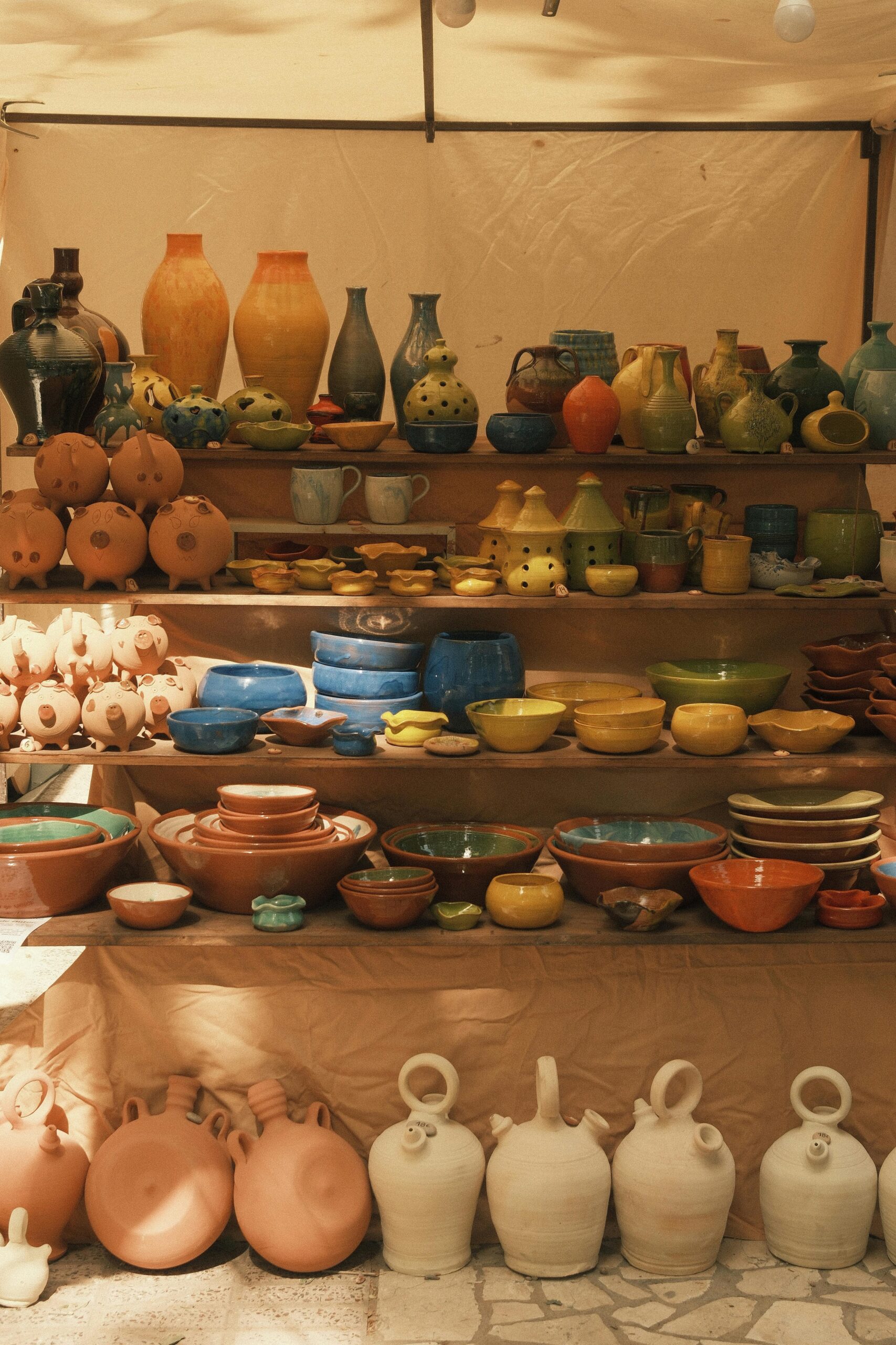 Vibrant handmade pottery arranged on wooden shelves at an outdoor bazaar.