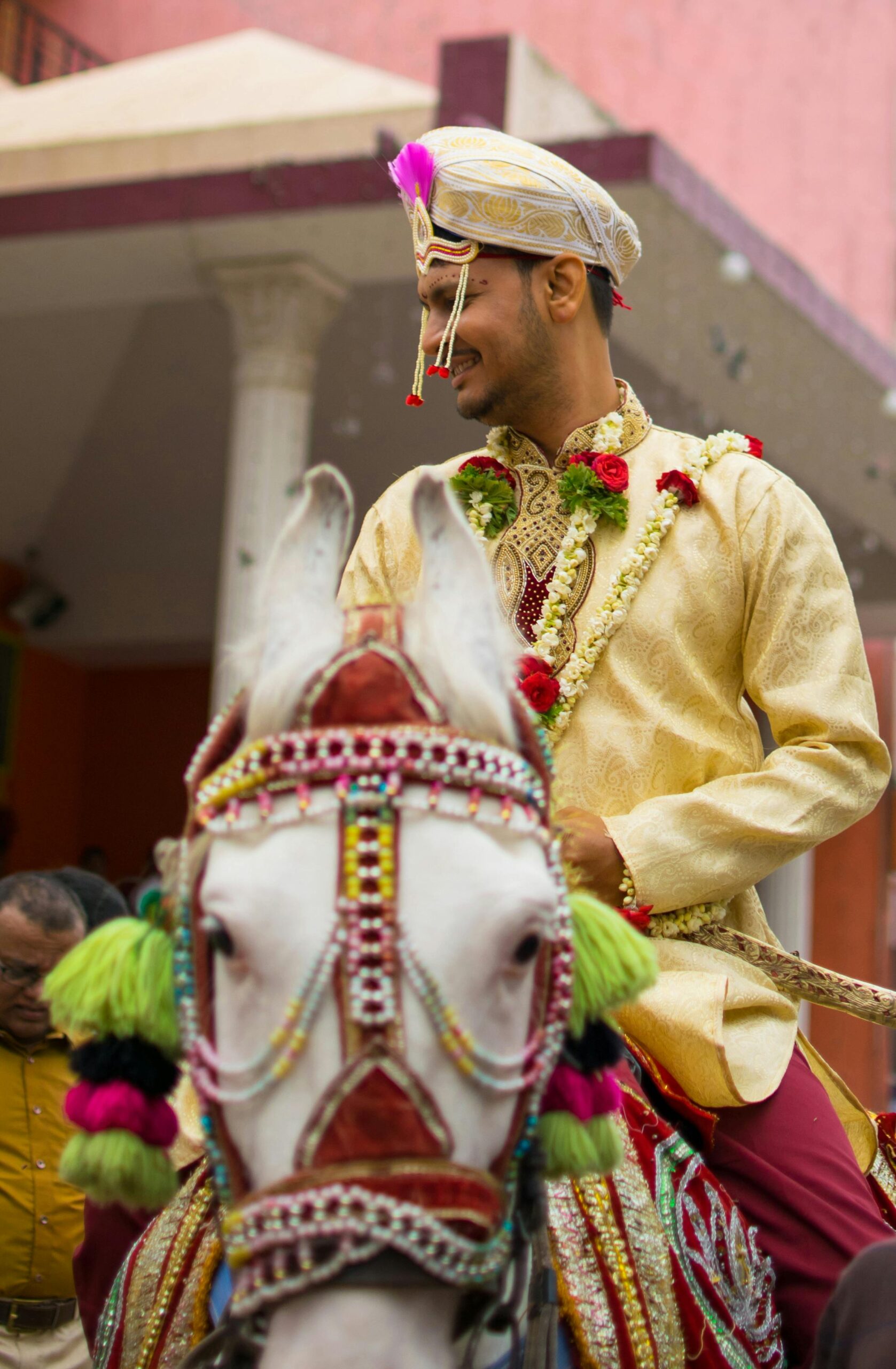 Indian groom in traditional attire riding a decorated horse during a vibrant wedding procession.